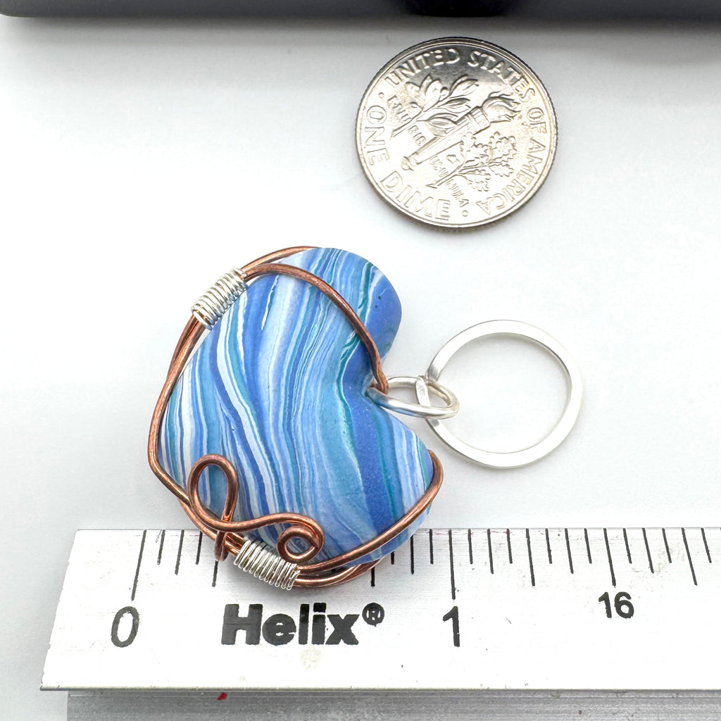 A heart-shaped marbled blue and white clay pendant wrapped in copper wire with a silver jump ring, shown next to a US dime for scale and a metal ruler marked Helix for scale.