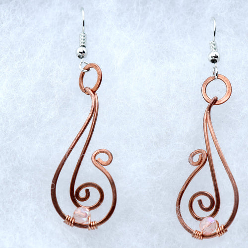 A pair of handmade copper wire dangle earrings with silver fishhook wires and small pink rose quartz beads, displayed on a textured white background.