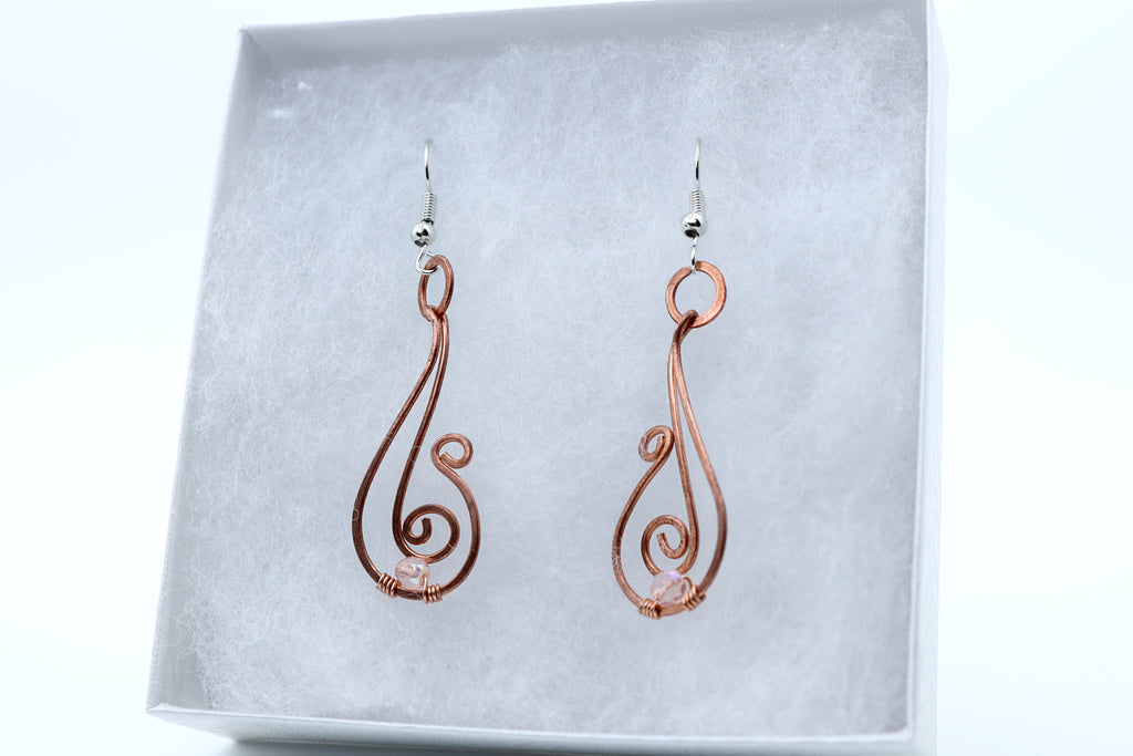 A pair of copper wire dangle earrings with silver fishhook backings, displayed inside a white jewelry box with a textured gray insert.
