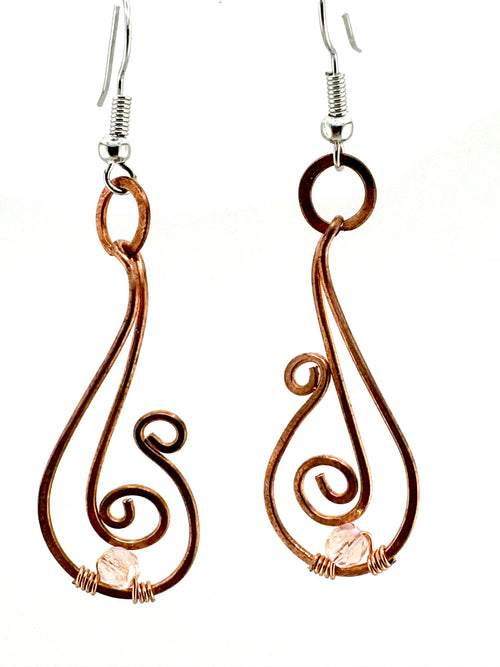 A pair of handmade wire earrings with copper-colored loops and swirls, featuring small pale pink gemstone accents and silver fishhook ear wires, shown against a plain white background.
