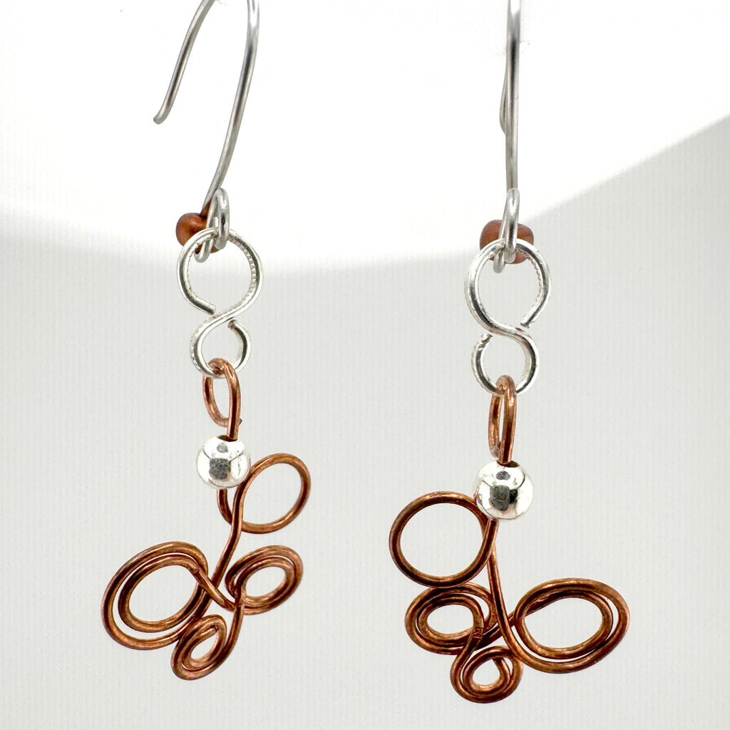 A pair of handmade wire earrings featuring copper-colored loops and silver-toned metal hooks and beads, displayed against a clean white background.