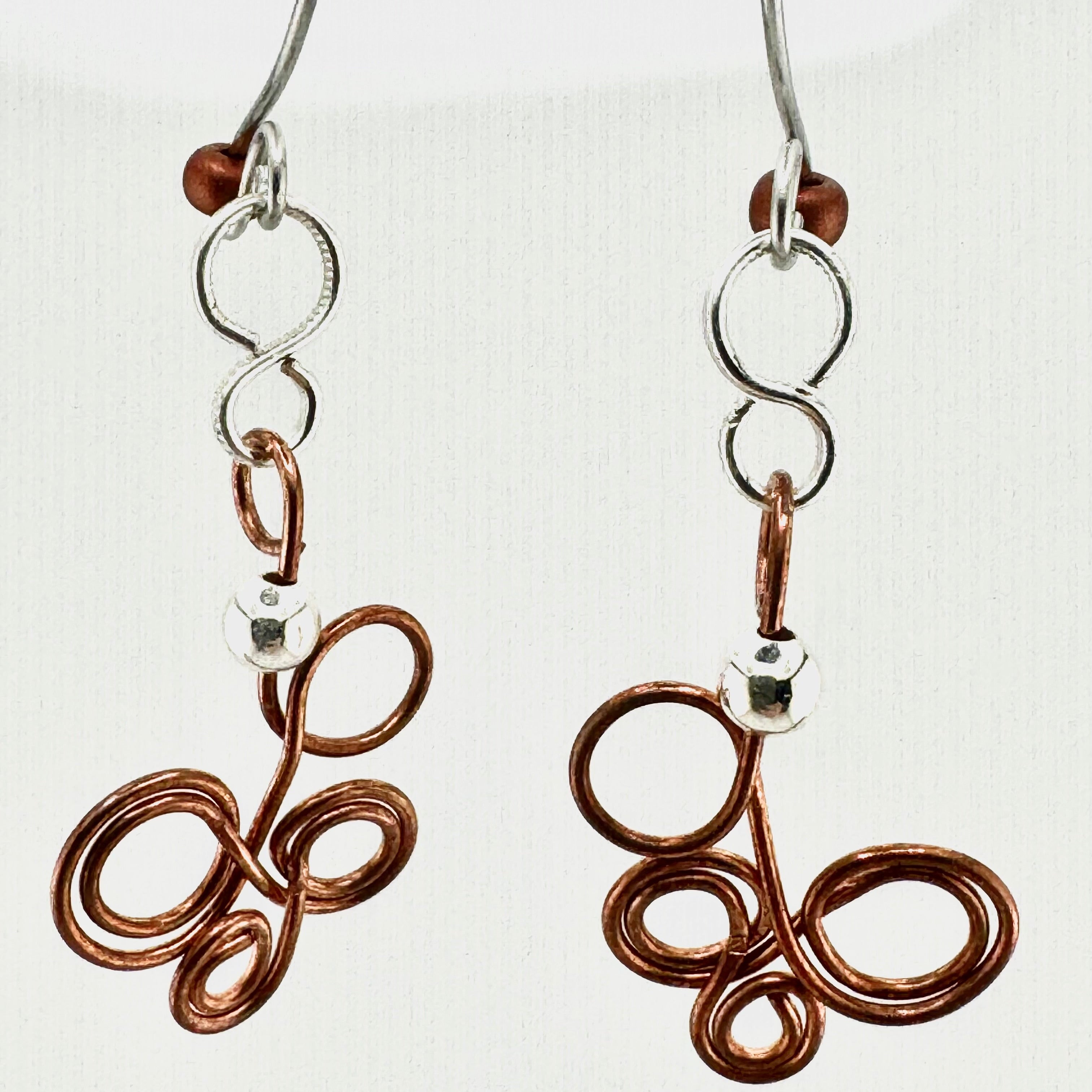 A pair of handmade wire earrings featuring copper-colored coiled loops and silver-tone metal hooks and beads, shown against a plain off-white background.