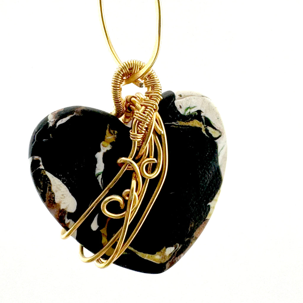 back of the heart-shaped marbled clay pendant wrapped in gold wire, hanging from a gold chain on a white background.