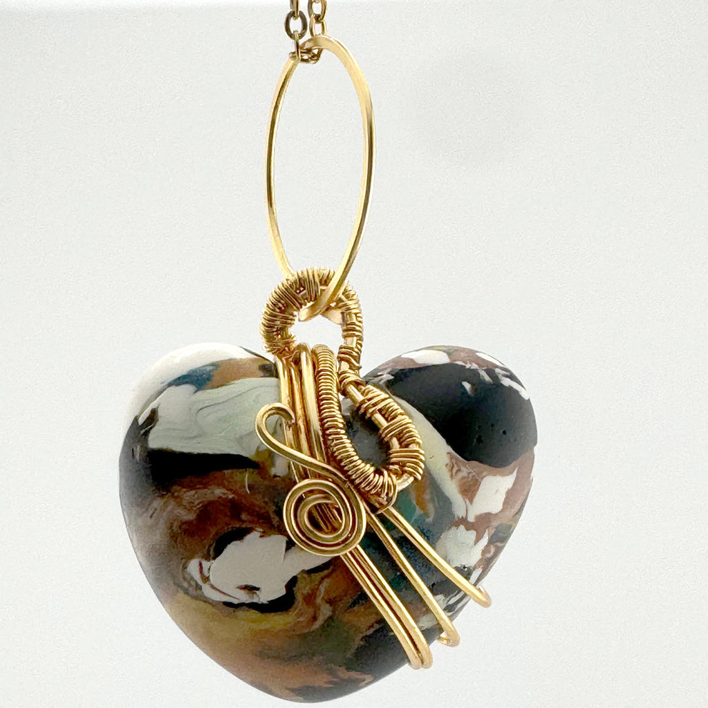 A heart-shaped clay pendant necklace with a gold wire-wrapped accent and a gold chain, shown against a plain white background.