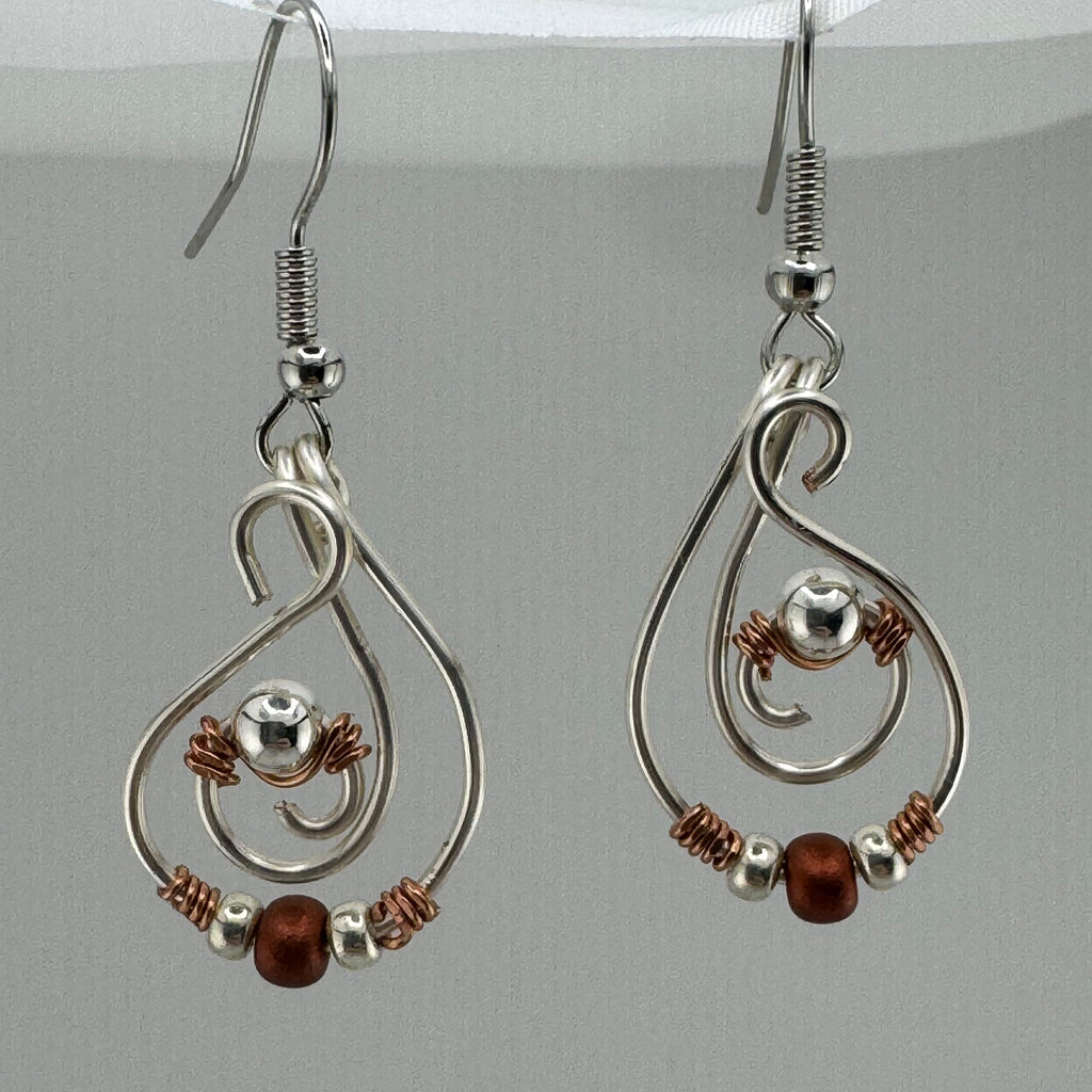A pair of silver-toned wire dangle earrings with copper wire accents, small silver beads, and copper beads, displayed against a light gray background.