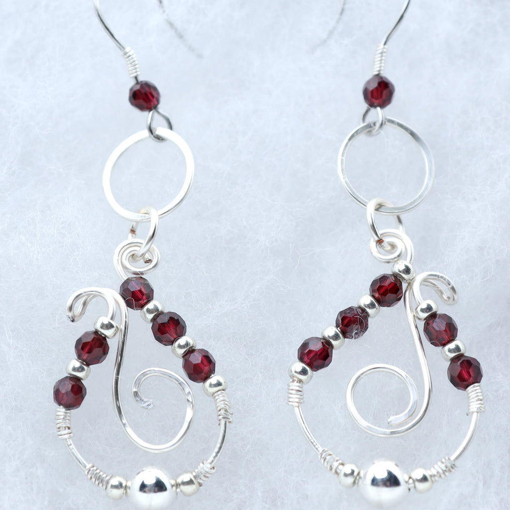 A pair of silver dangle earrings with faceted dark red garnets, displayed on a light textured background.