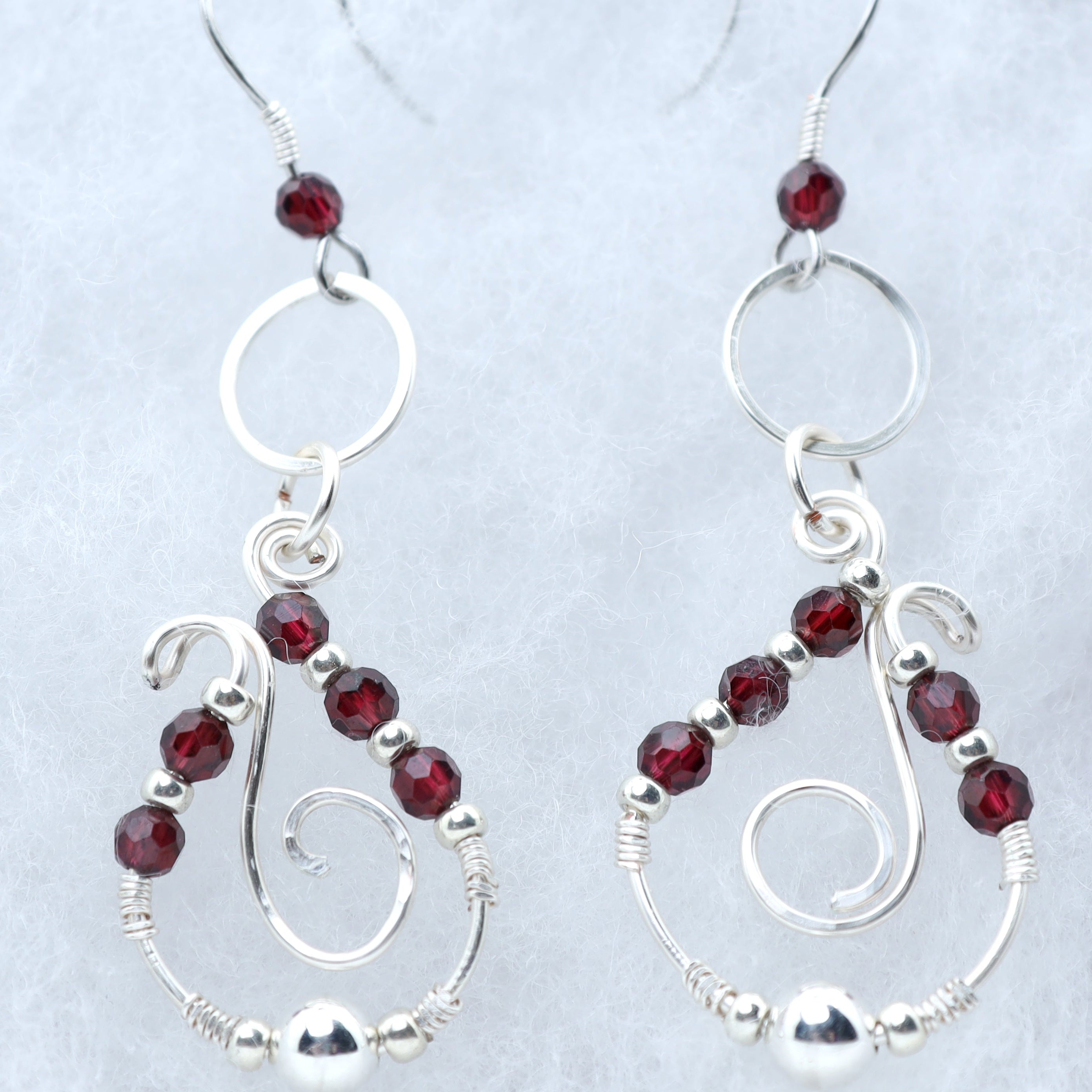 A pair of silver dangle earrings with faceted dark red garnets, displayed on a light textured background.
