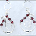 A pair of silver dangle earrings with faceted dark red garnet gemstone beads and silver wire swirls, displayed on a light textured background.