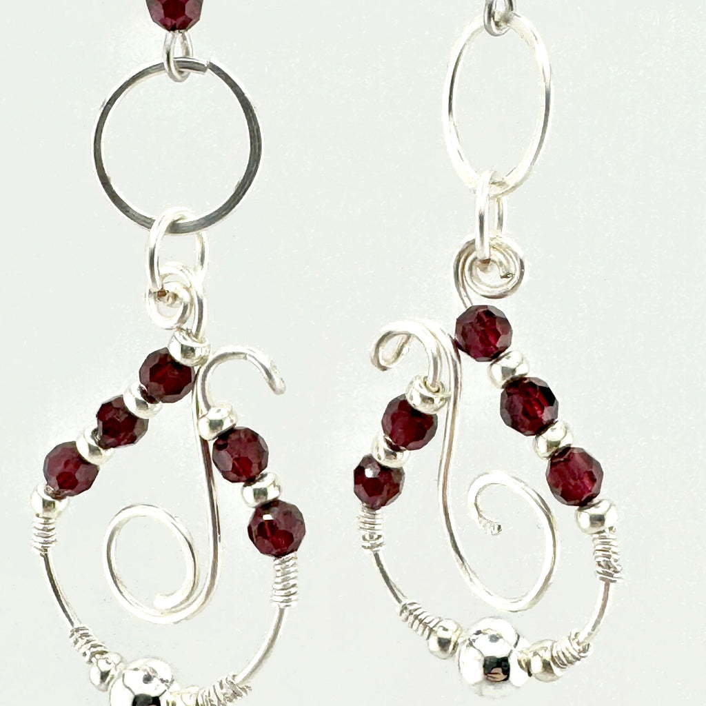 A pair of silver wire-wrapped drop earrings with faceted dark red garnet stones, shown against a plain white background.