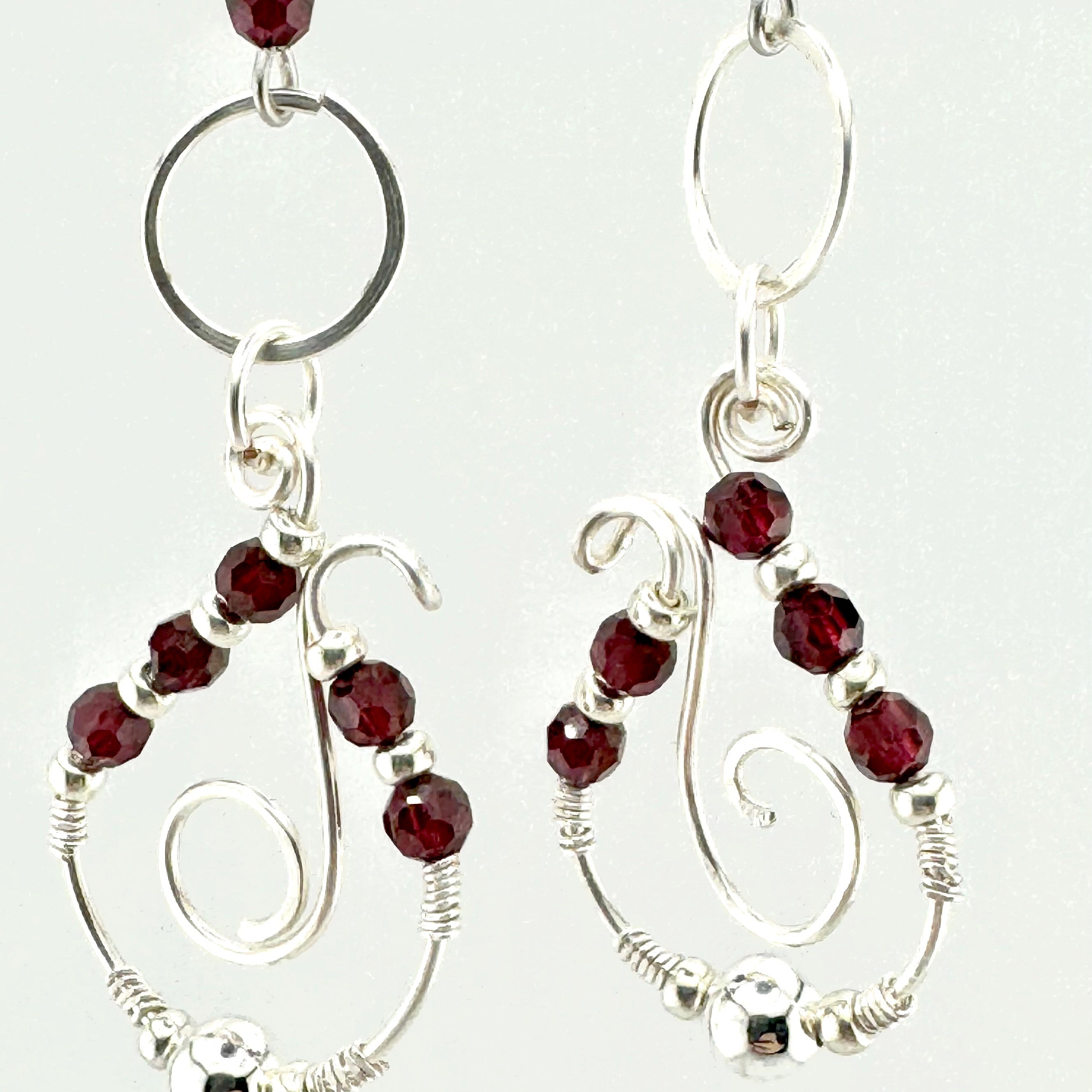 A pair of silver wire-wrapped drop earrings with faceted dark red garnet stones, shown against a plain white background.