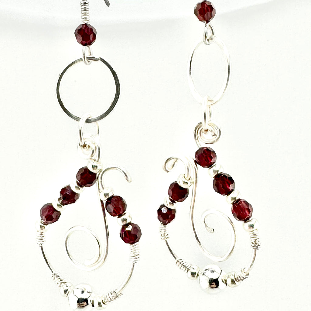 A pair of silver-toned dangle earrings with faceted dark red garnets, featuring circular and spiral wire designs on a white background.