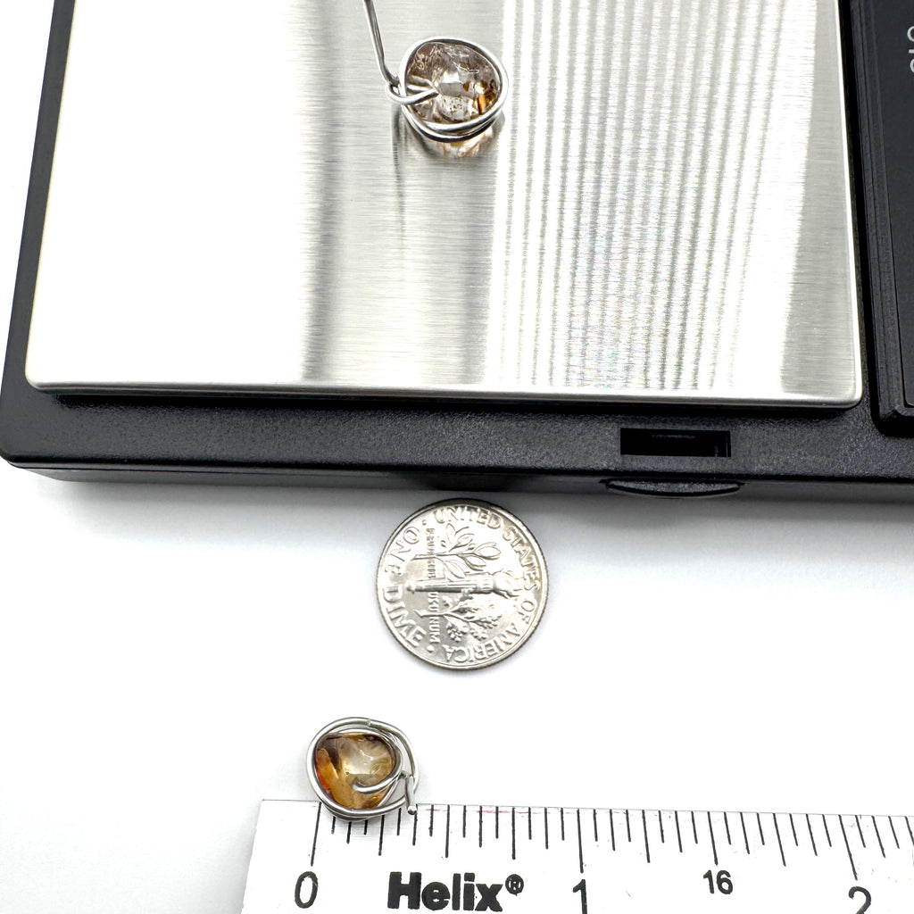 Stainless steel wrapped quartz stones with warm golden-brown natural inclusions stud earrings
are shown on a white surface with a coin and ruler for scale, with part of a digital scale visible at the top.