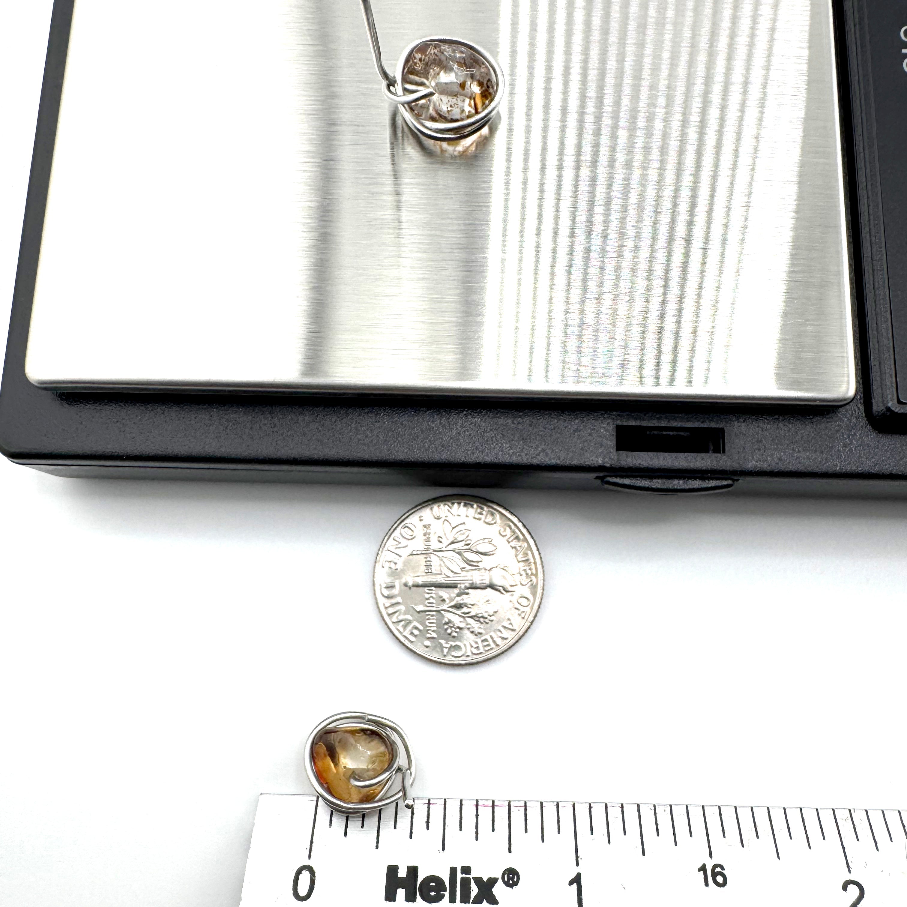 Stainless steel wrapped quartz stones with warm golden-brown natural inclusions stud earrings
are shown on a white surface with a coin and ruler for scale, with part of a digital scale visible at the top.