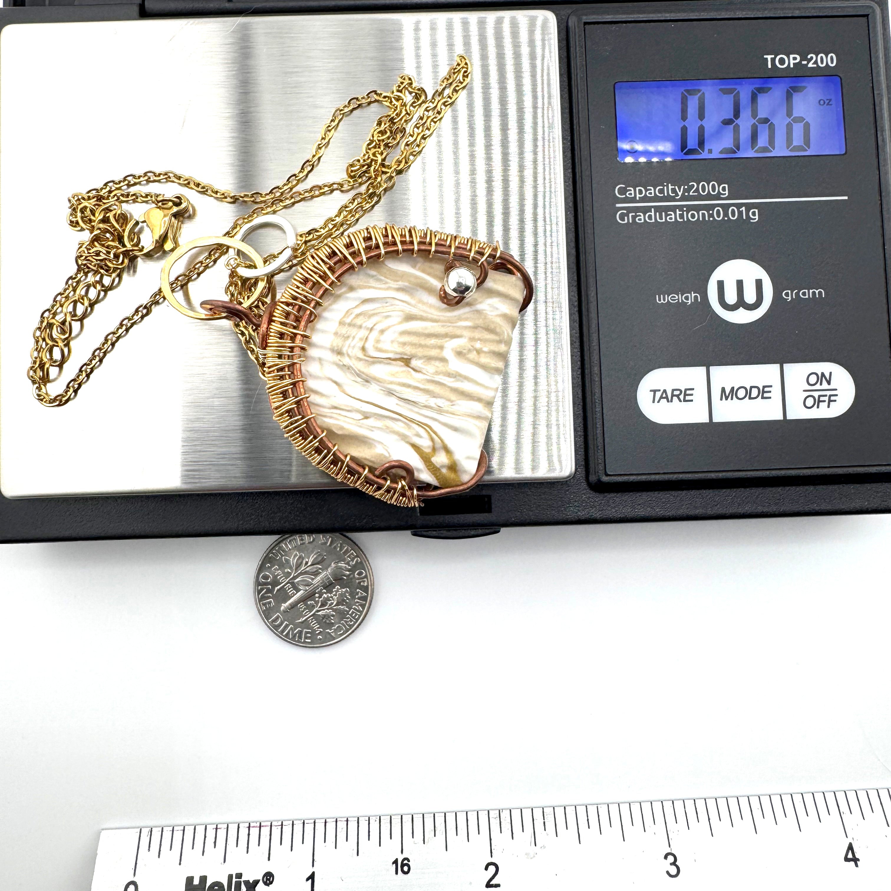A gold chain necklace with a large clay pendant is shown resting on a digital scale, with a dime and ruler below for scale. The scale display reads .366 oz.