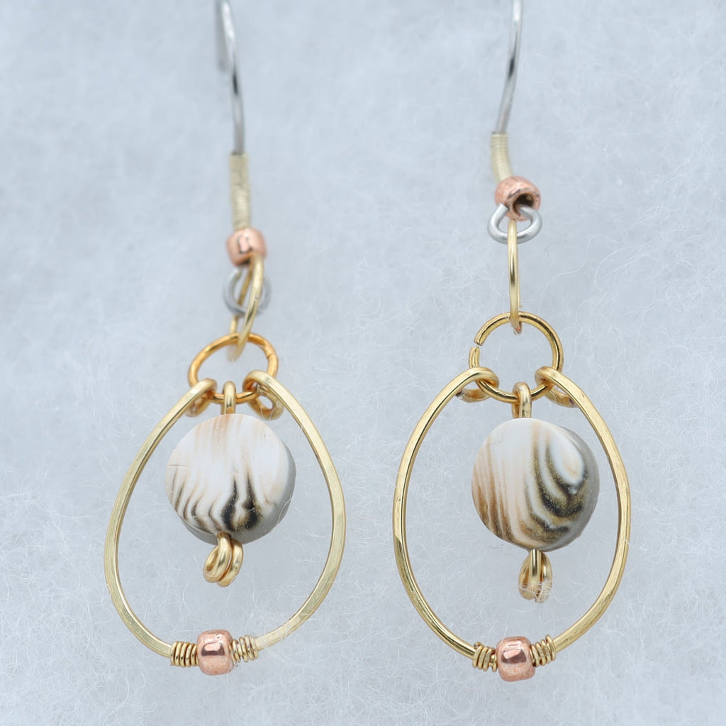 A pair of gold and rose gold drop earrings with white, tan and gray marbled clay beads, displayed on a light gray velvet jewelry box.