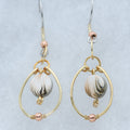 A pair of gold and rose gold drop earrings with white, tan and gray marbled clay beads, displayed on a light gray velvet jewelry box.