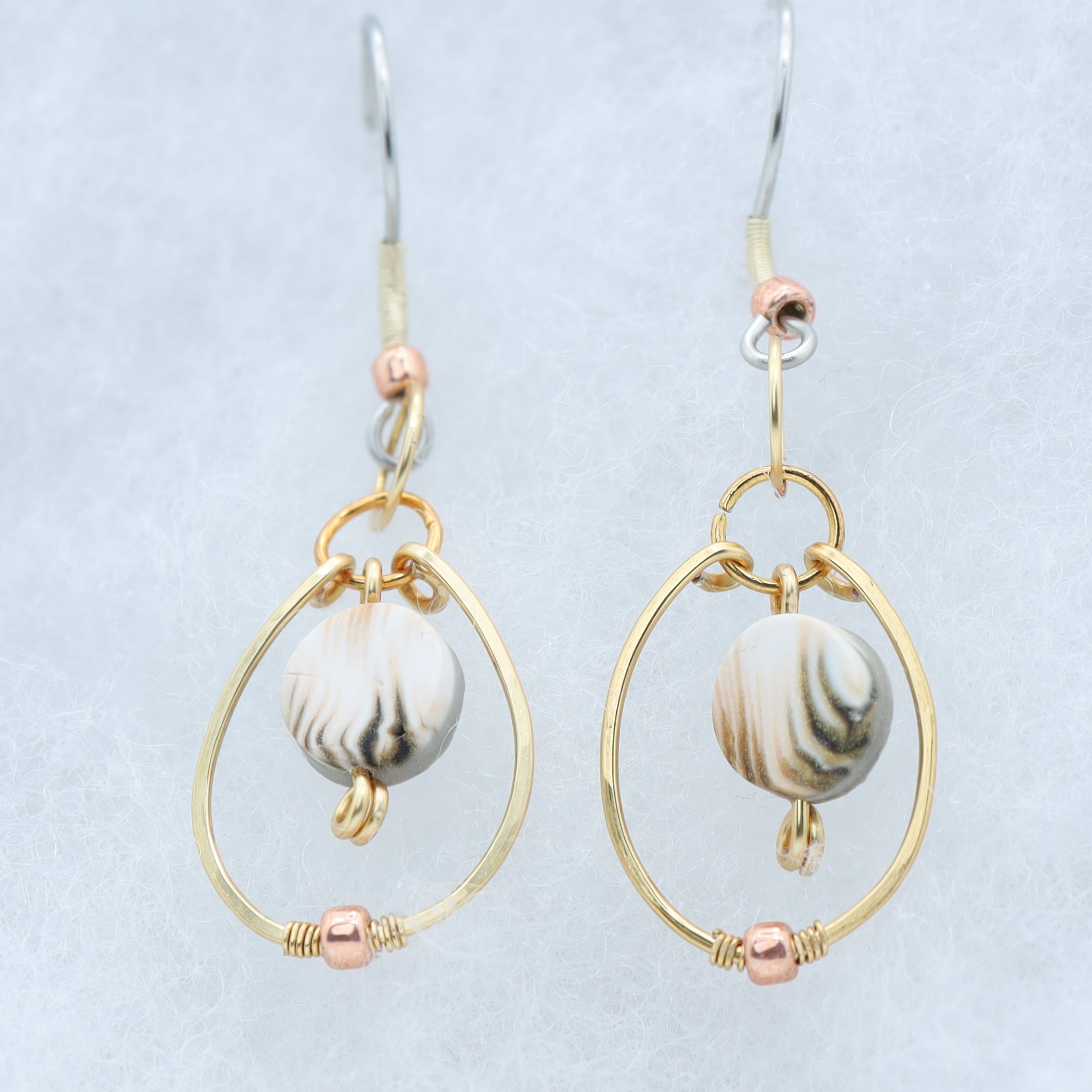 A pair of gold and silver dangle earrings with white and gray marbled clay beads, displayed on a light gray textured background.
