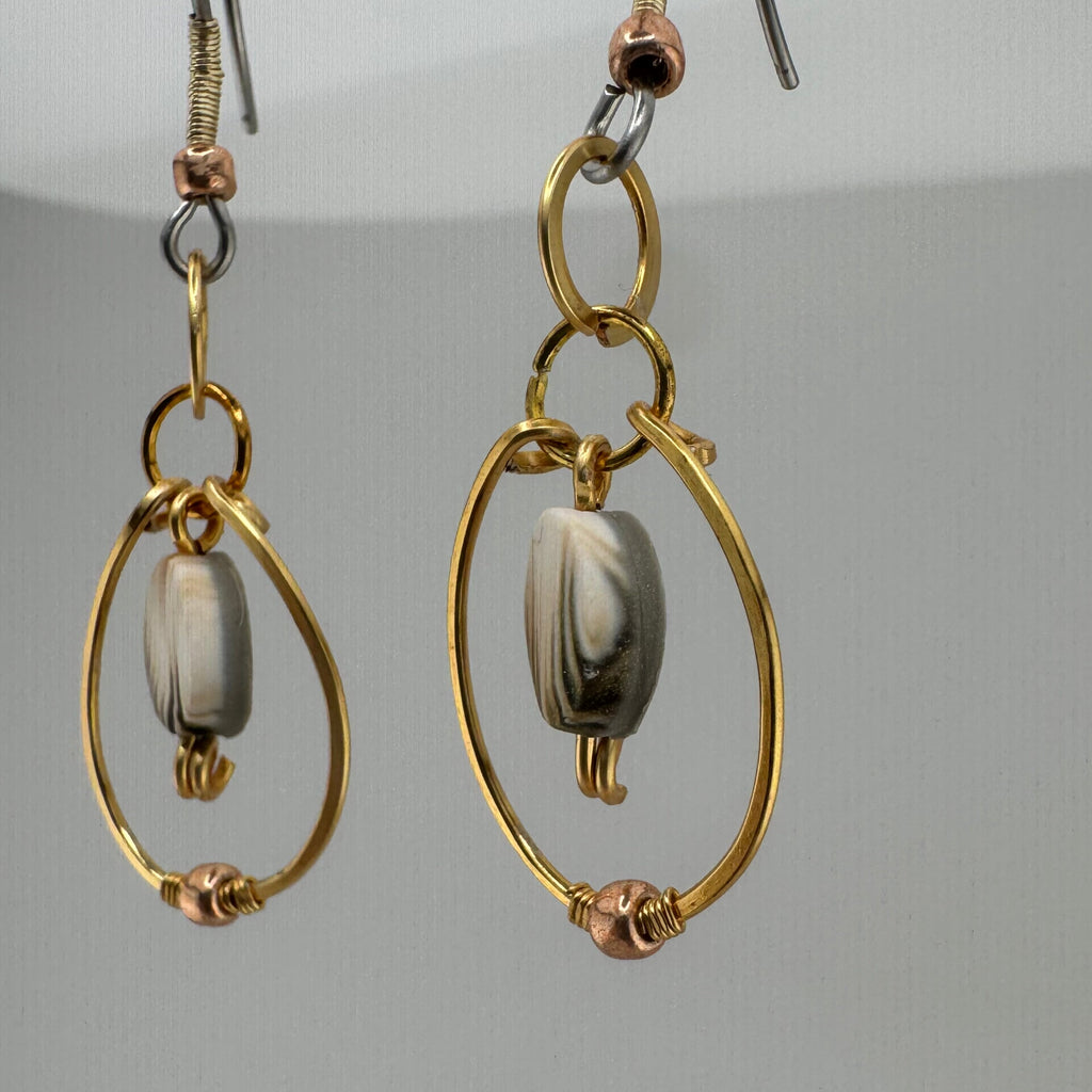 Side view of a pair of gold and  silver wire-wrapped dangle earrings with oval bezel-set gray beads, shown against a neutral light gray background.