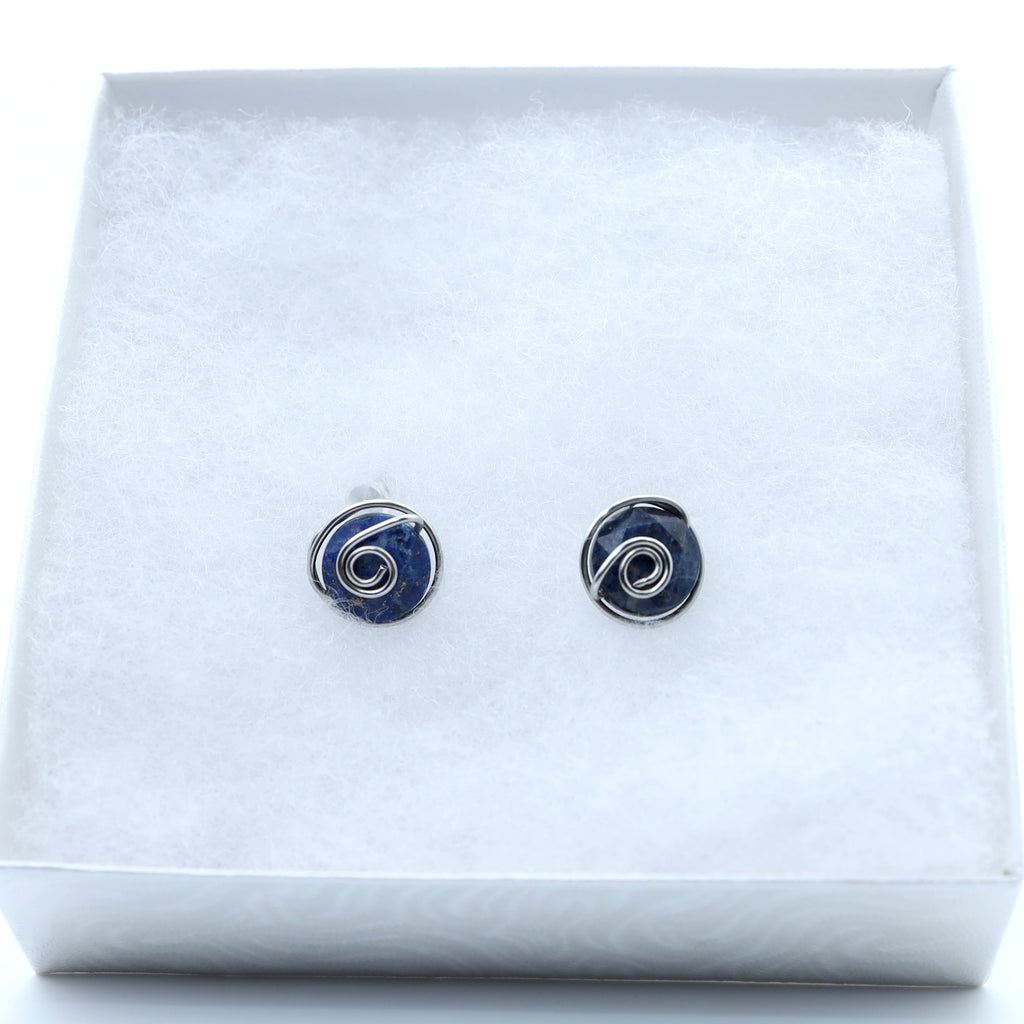 A pair of small  stud earrings featuring dark blue aventurine 10mm faceted stones held in hand-shaped stainless steel spiral wire details,, displayed on a white textured insert inside a white gift box.