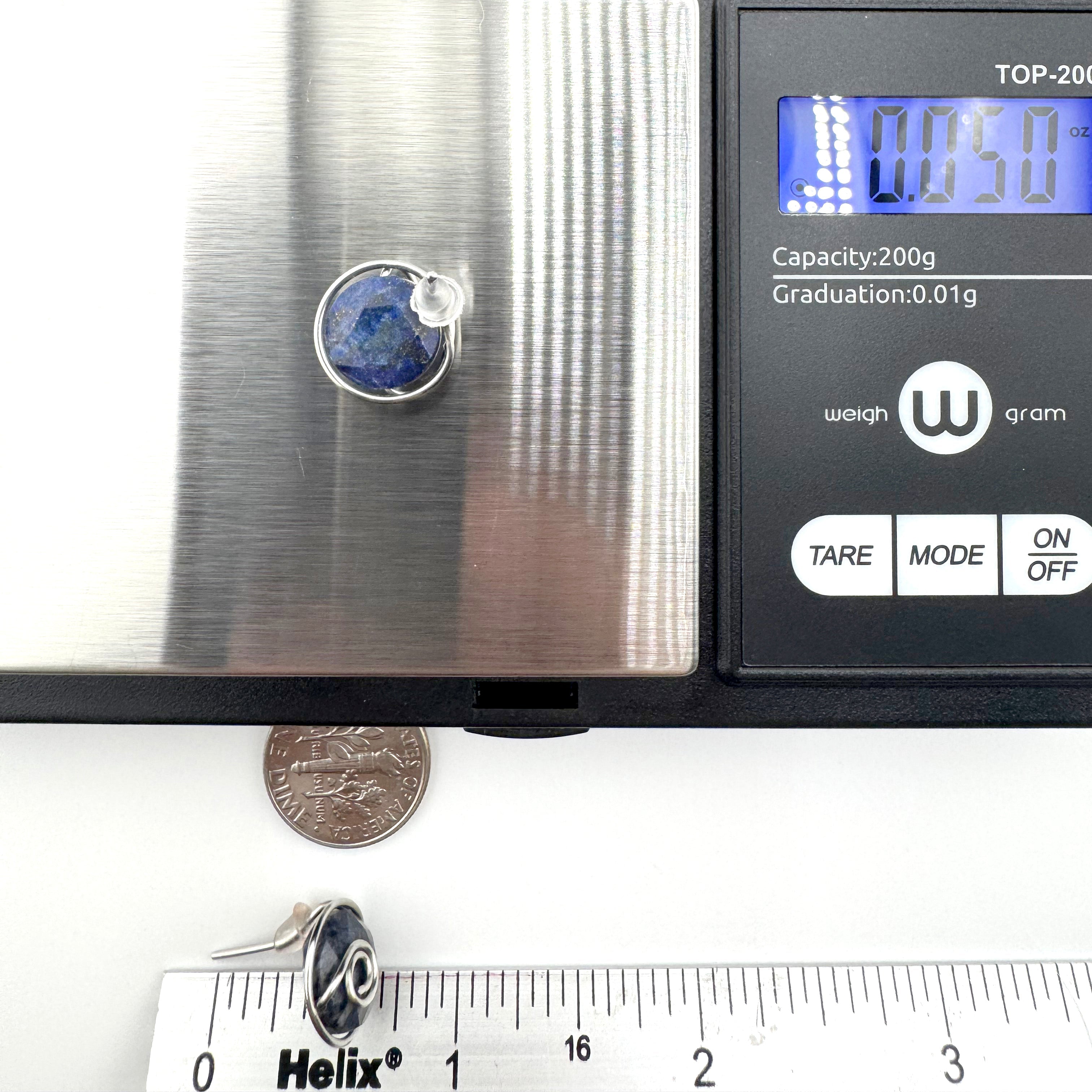 A pair of  wire-wrapped earrings featuring dark blue aventurine 10mm faceted stones held in hand-shaped stainless steel spiral wire details on a digital scale reading 0.050 g, with a dime and ruler below for scale.