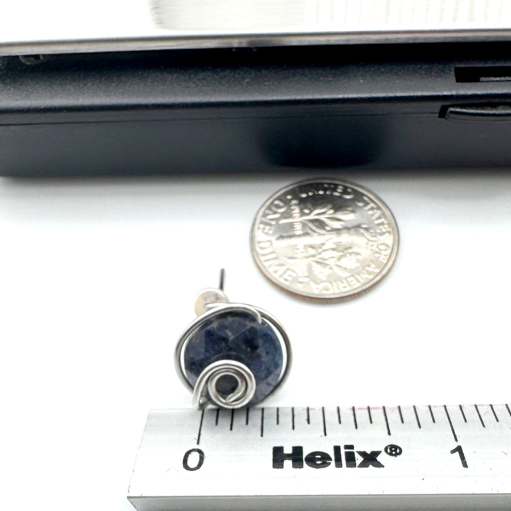 A small  stud earring  featuring dark blue aventurine 10mm faceted stones held in hand-shaped stainless steel spiral wire details, shown next to a dime and a Helix ruler for scale on a white background.