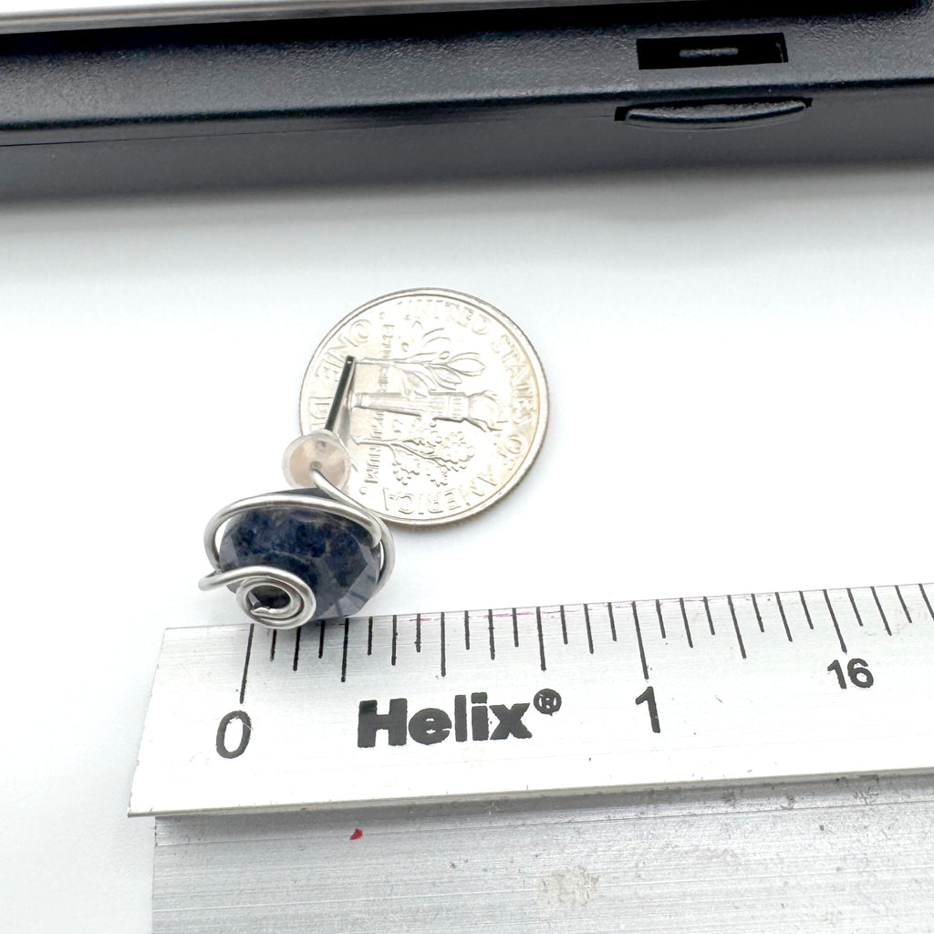 A pair of  wire-wrapped earrings featuring dark blue aventurine 10mm faceted stones held in hand-shaped stainless steel spiral wire details, shown next to a US quarter for scale and a Helix ruler on a white surface.