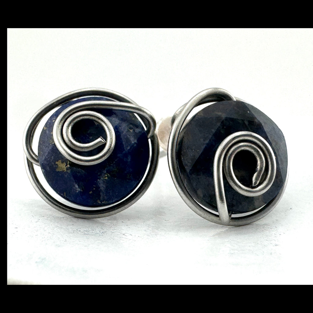 A pair of handmade wire-wrapped earrings featuring dark blue aventurine 10mm faceted stones held in hand-shaped stainless steel spiral wire details, set against a plain white background.