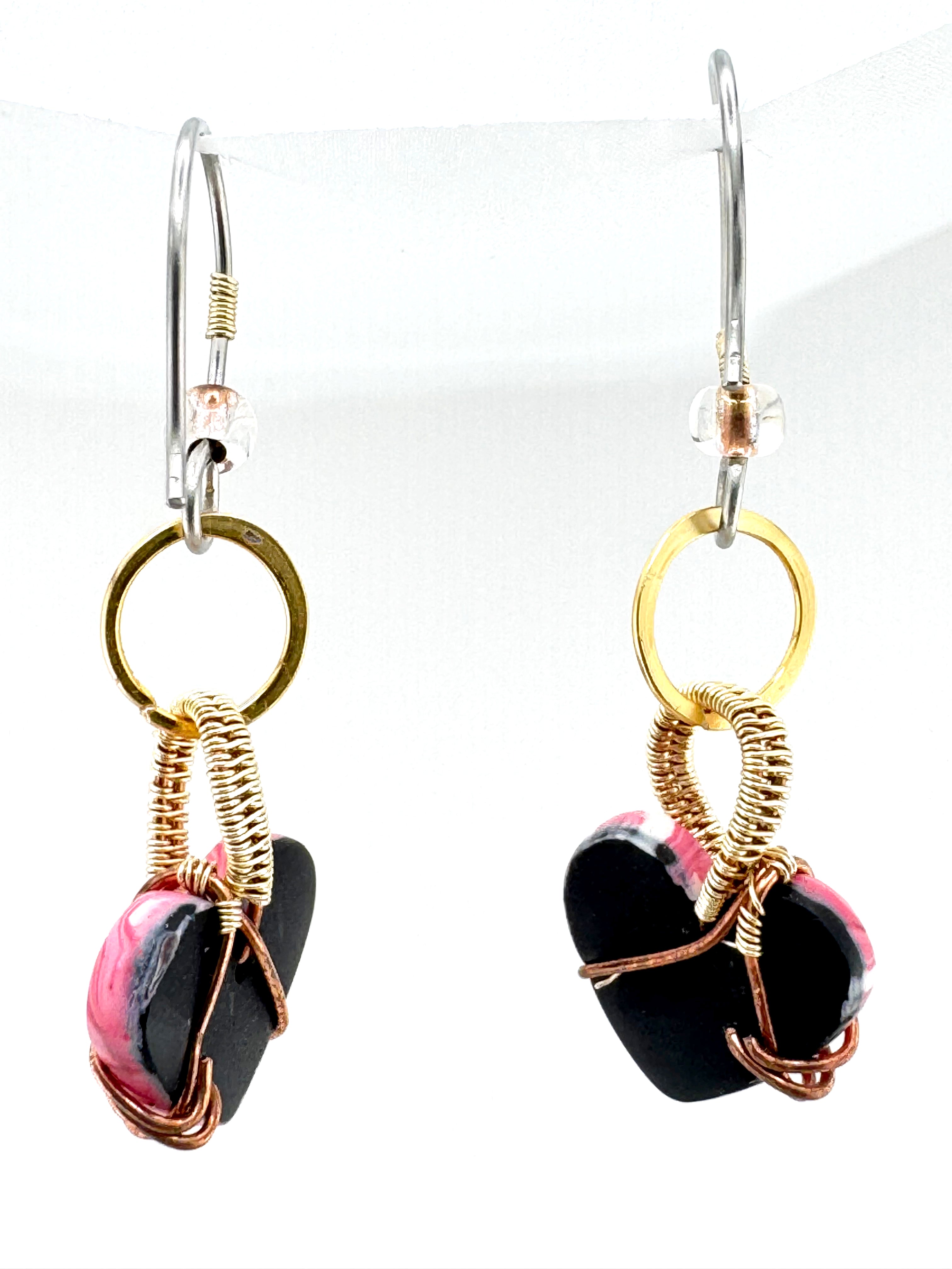 back view of a pair of handmade dangle earrings featuring polished white and pink heart-shaped clay beads wrapped in copper wire, suspended from gold-toned rings on silver-toned French hook ear wires, shown against a plain white background. 
