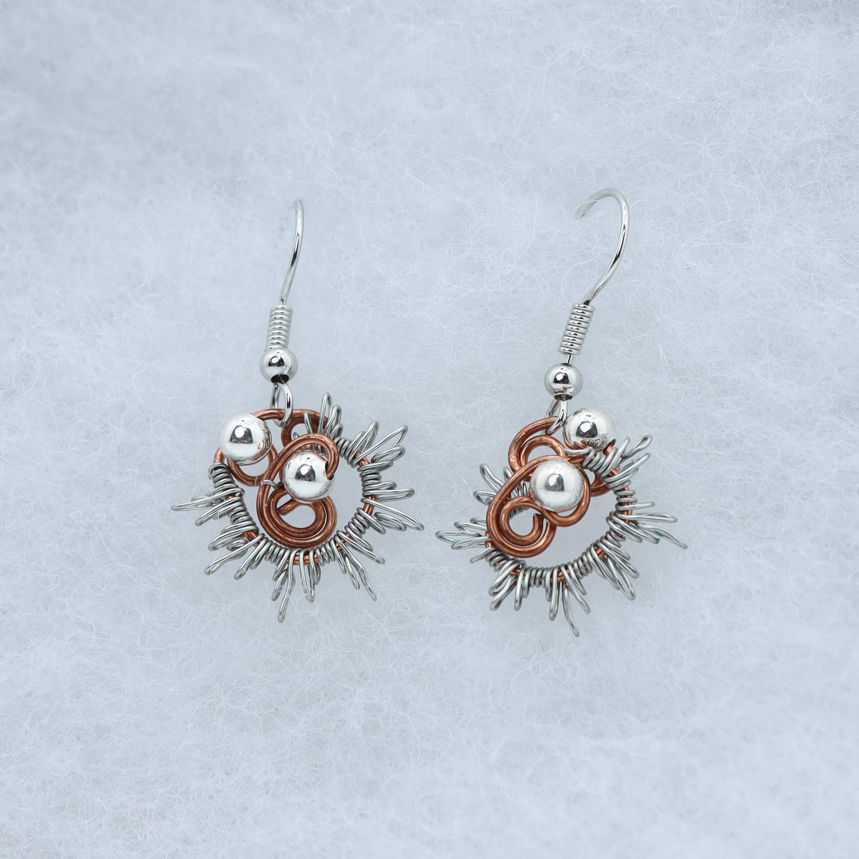 Earrings feature a textured silver-colored wire frame with lively copper swirls and polished silver-toned beads. The design has an energetic, almost crown-like shape.