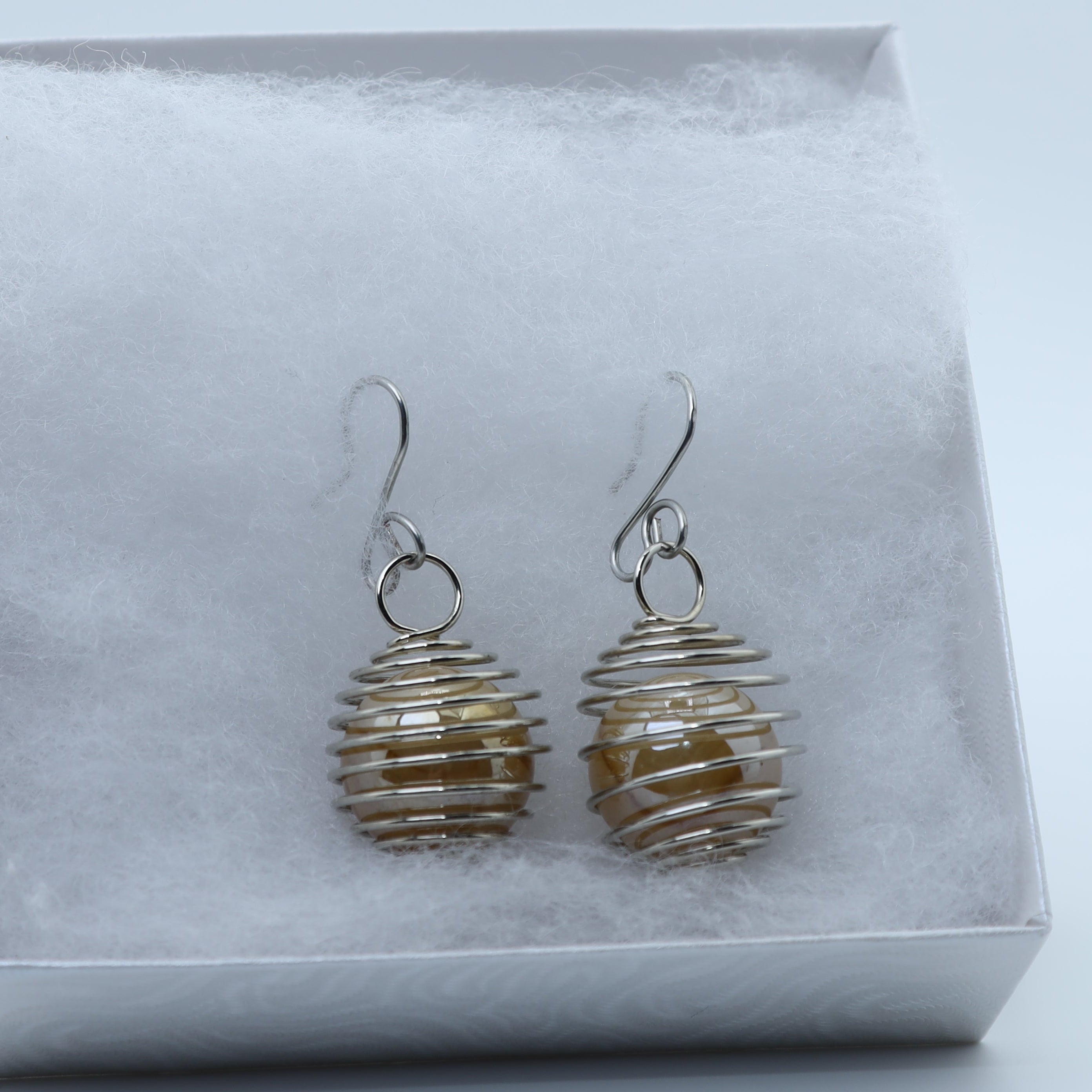 A pair of silver wire-wrapped dangle earrings with amber-colored beads, presented in a white gift box with white foam insert.