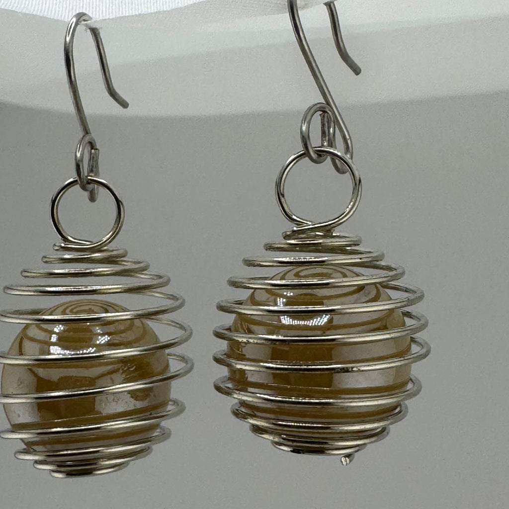 A pair of handmade dangle earrings featuring a silver-colored coiled wire design wrapping around a smooth, oval, translucent brown bead, suspended from silver hooks against a neutral light gray background.