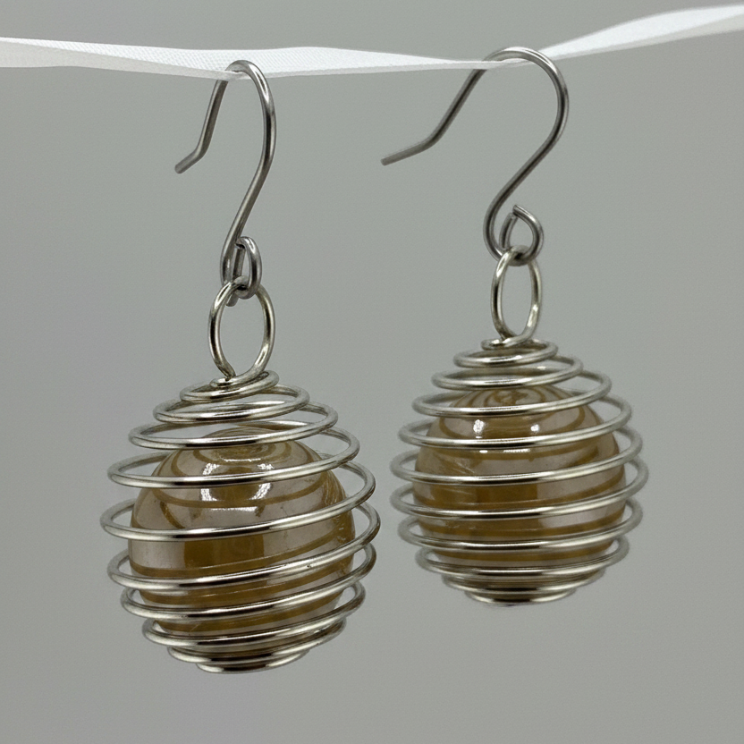 A pair of silver wire spiral drop earrings with smooth, translucent amber-brown beads inside, hanging from silver hooks against a neutral gray background.