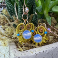 Gold wire-wrapped earrings with clear glass beads in a pot with plants