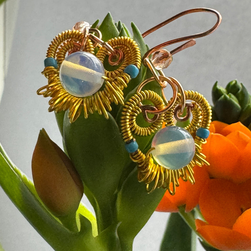 Gold wire-wrapped earrings with a central glass bead on a leafy background