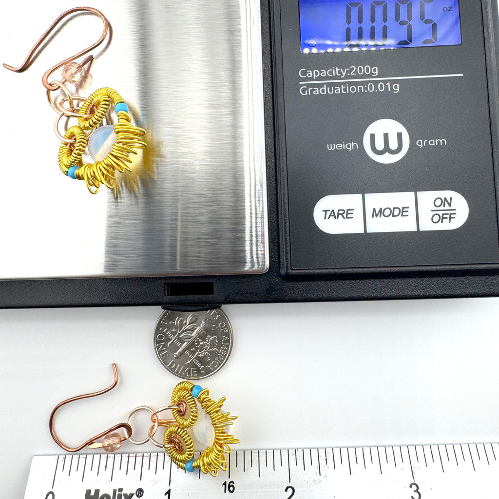 A pair of gold and copper spiral dangle earrings with light blue accents, shown on a digital scale and next to a dime and ruler for scale. 